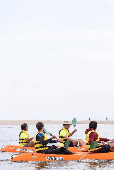 Four people in a small orange boat on a body of water, wearing life jackets and paddles. 5
