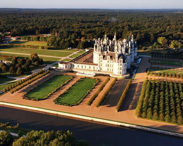 A grand castle surrounded by meticulously maintained gardens and a river. 1