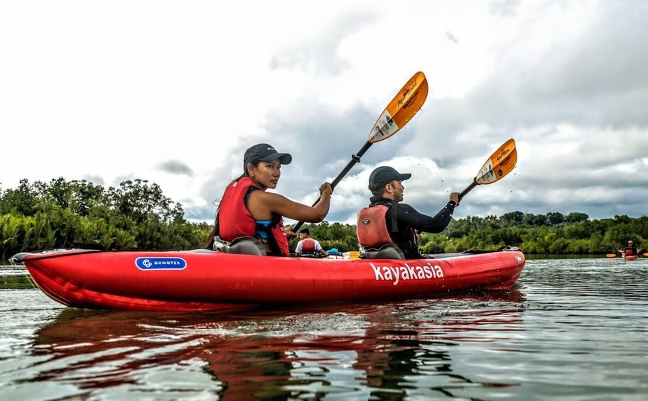 Two people kayaking in a red kayak on a calm river with trees in the background. 5