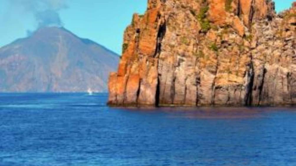 A rocky coastline with a prominent cliff and a distant volcano. 2