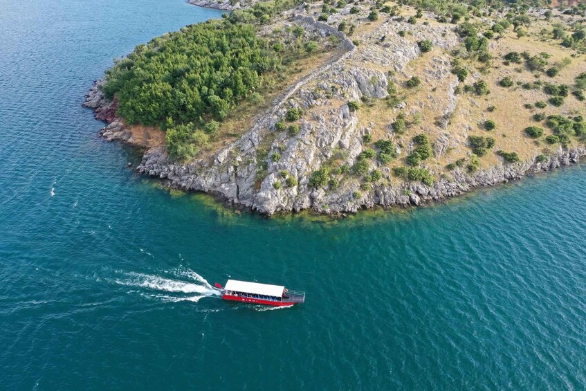 A boat on a turquoise sea, a rocky island with sparse vegetation, and a clear sky. 2