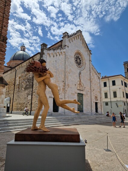 A sculpture of a man and woman in an embrace, a church with a dome and rose window, and a clear blue sky with clouds. 2