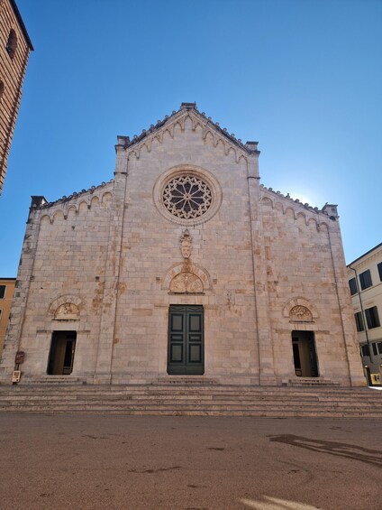 A historic stone building with a large circular window and two green doors. 1