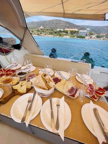 A table set for a meal with various cheeses, meats, and bread, overlooking a coastal landscape with buildings and hills. 3