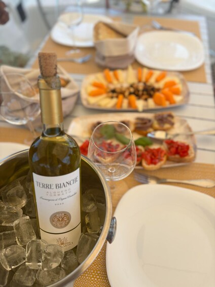 A bottle of Terre Bianche wine on ice, surrounded by plates of food and a wine glass. 4