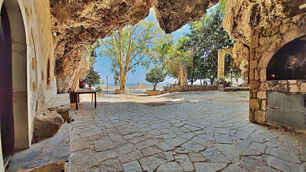 A stone-paved courtyard with a rustic archway, a small table, and a view of the sea. 1