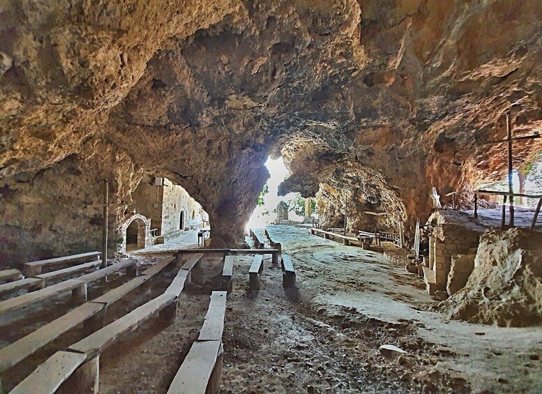 A cave with a large opening, stone benches, and a pathway leading to a distant view. 4