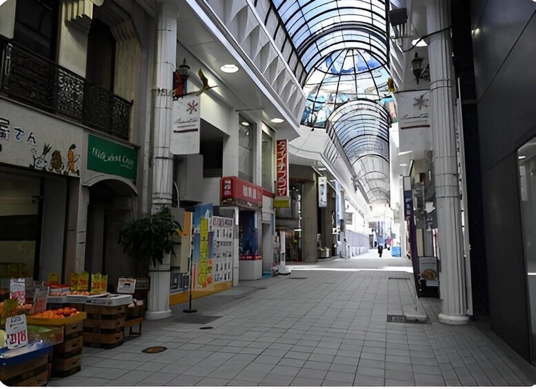 An indoor shopping mall with a glass ceiling, white columns, and various shops. 1