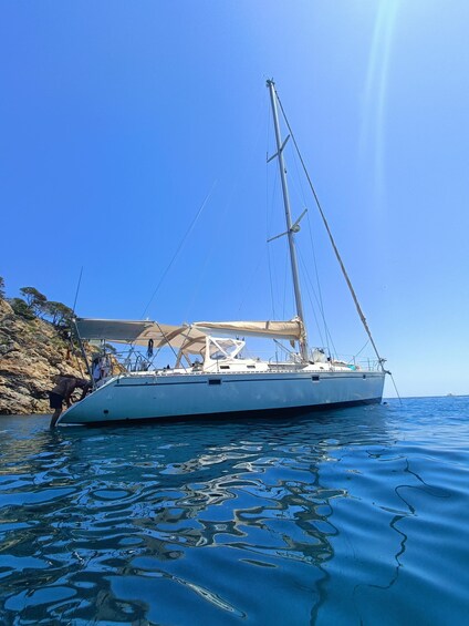 A sailboat anchored near a rocky coastline. 1