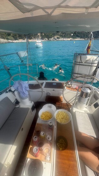 A boat's deck with snacks and drinks, a steering wheel, and a view of swimmers in the water. 4