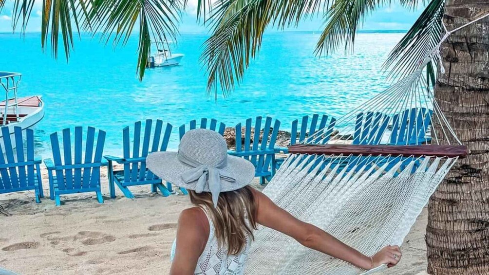 A person relaxing on a hammock by a beach with turquoise water and a boat in the distance. 4