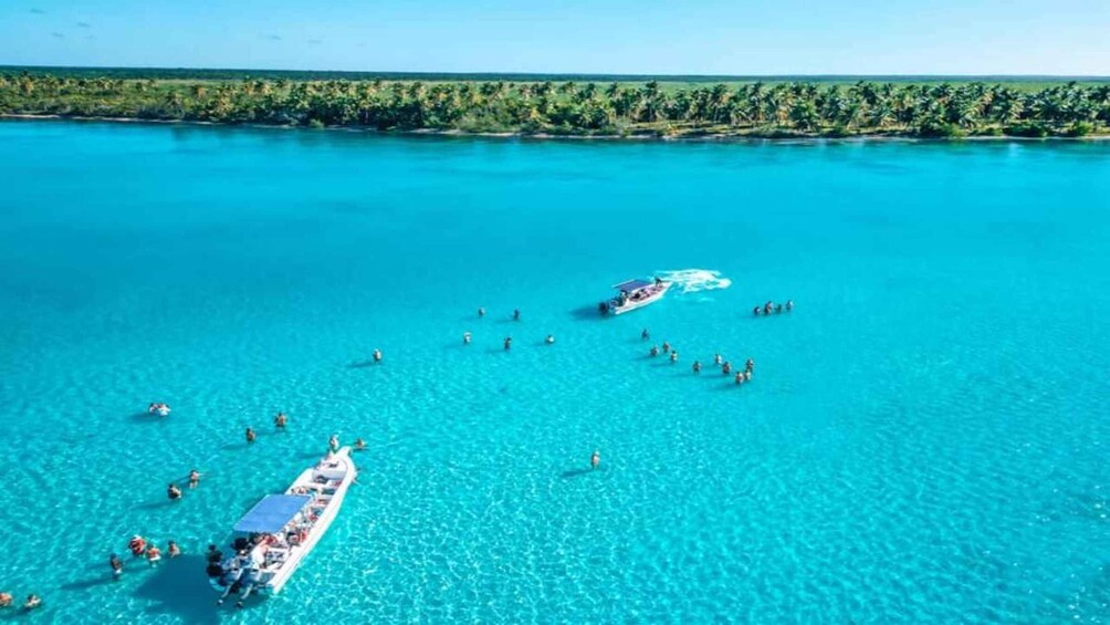 A clear turquoise sea with a boat carrying passengers, surrounded by a dense tropical shoreline. 5