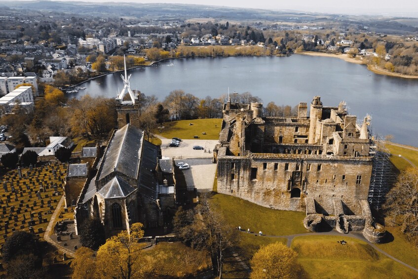 A historic castle by a river, surrounded by a cemetery and a town. 3