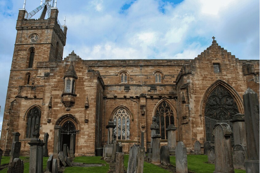 A historic church with a clock tower, arched windows, and a graveyard in front. 5