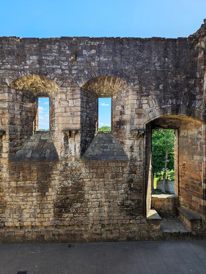 An ancient stone wall with arched openings and a doorway leading to a lush green garden. 2