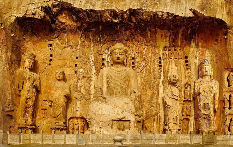 A large Buddha statue surrounded by smaller statues, set against a textured wall. 1
