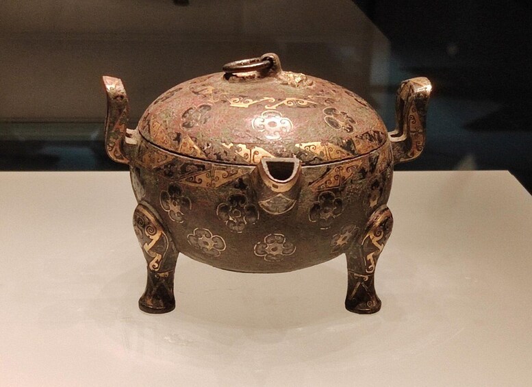 A bronze tripod cauldron with intricate designs and a central handle. 5