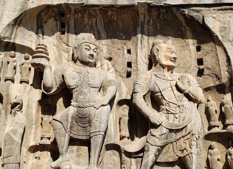 A detailed stone carving of two figures in traditional attire, set against a rock face with a large archway. 3