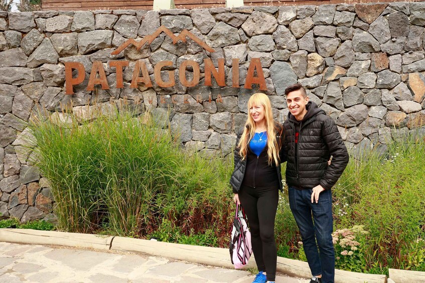 A stone wall with the sign 'Patagonia' and two people standing in front of it. 2