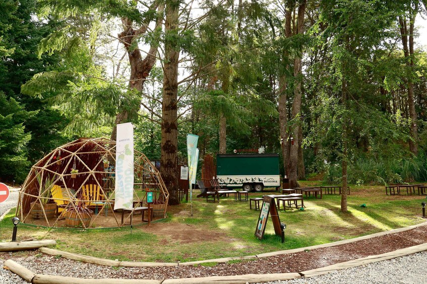 A geodesic dome structure, picnic tables, a truck, and a signboard in a forested area. 3