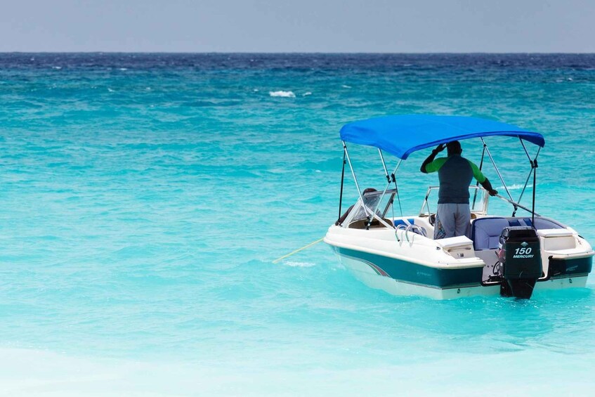 A person on a small boat with a blue canopy, a motor labeled '150 MERCURY,' and calm turquoise waters. 2