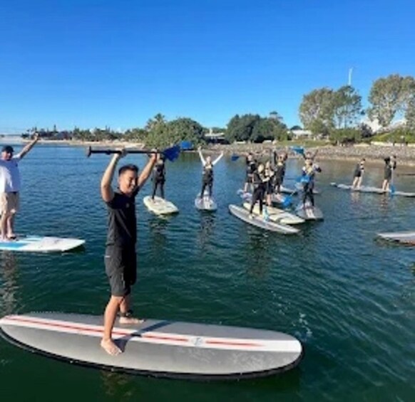 People paddleboarding on a calm body of water with trees and a clear sky in the background. 2