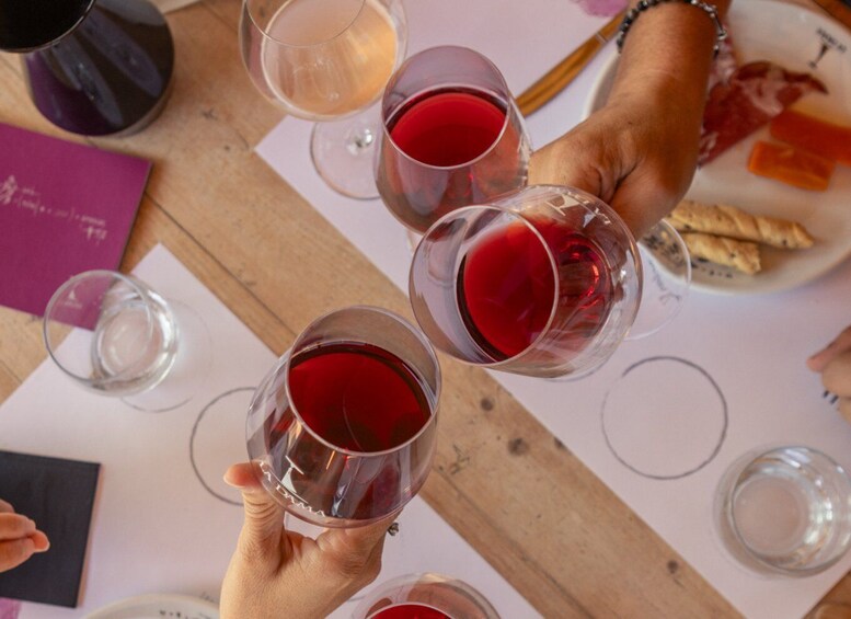 A group of people holding wine glasses filled with red wine, with a wooden table and some food items in the background. 3