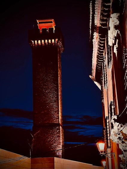 A tall, illuminated tower with a red top, surrounded by buildings with decorative lighting. 3
