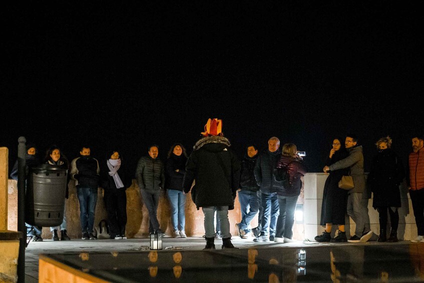 A group of people standing in a line on a sidewalk at night. 5