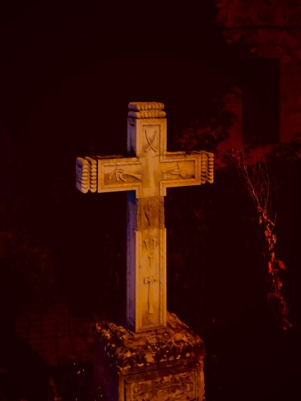 A stone cross with intricate carvings, set against a dark background with red lighting. 1