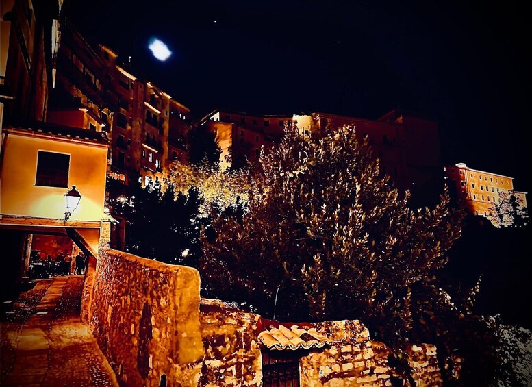A nighttime street scene with illuminated buildings and a tree. 4