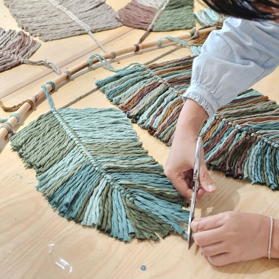 A person cutting a fringed textile with scissors on a wooden surface. 2