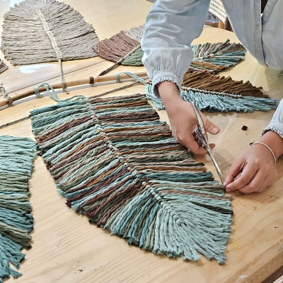 A person weaving a colorful macramé piece on a wooden table. 3