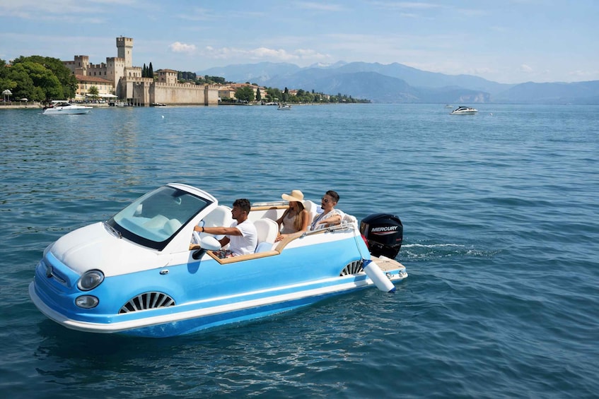 A small blue and white boat with passengers on a calm lake, with a castle and mountains in the background. 3