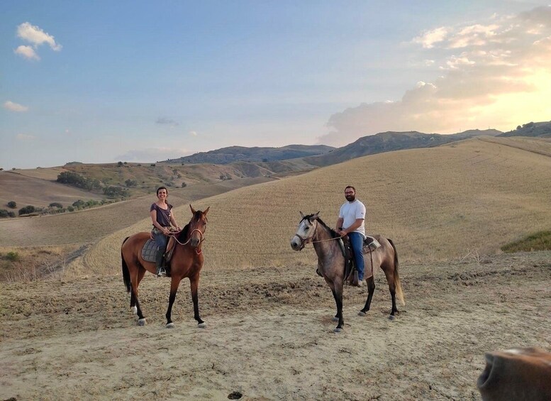 Two people riding horses on a dry, hilly landscape with rolling hills in the background. 1
