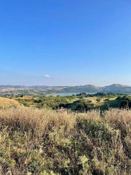 A landscape with rolling hills, a clear blue sky, and a distant body of water. 2
