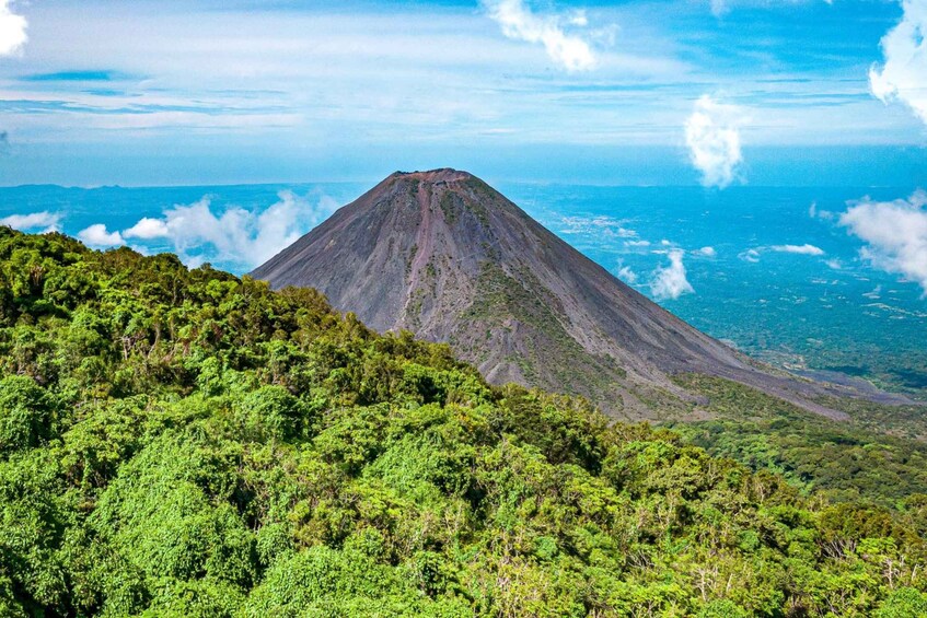A mountain with a conical peak, surrounded by dense green forest. 5