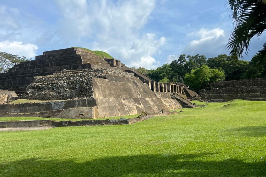 A large ancient pyramid with a stepped structure, surrounded by a grassy area and trees. 2