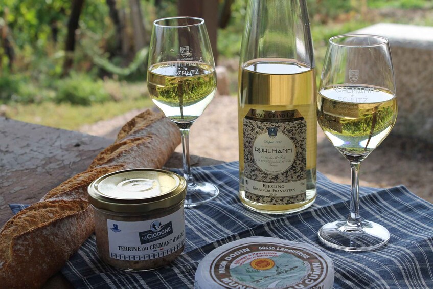 A picnic setup with a baguette, a bottle of Riesling wine, two glasses, and a jar of terrine. 3