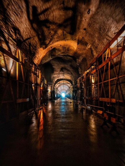 A dimly lit, arched tunnel with metal railings and a wet floor. 2