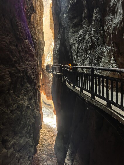 A narrow canyon with a wooden walkway and a person standing on it. 4