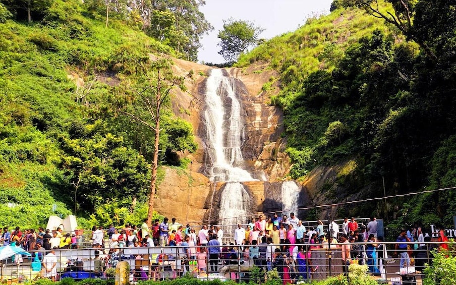A waterfall surrounded by lush greenery and a crowd of people. 2
