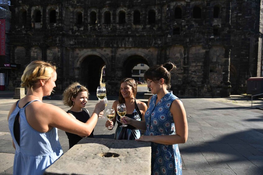 Four women toasting with wine glasses in front of a historic stone archway. 3