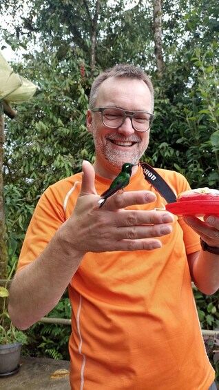 A person in an orange shirt holding a red object with a hummingbird on it. 3