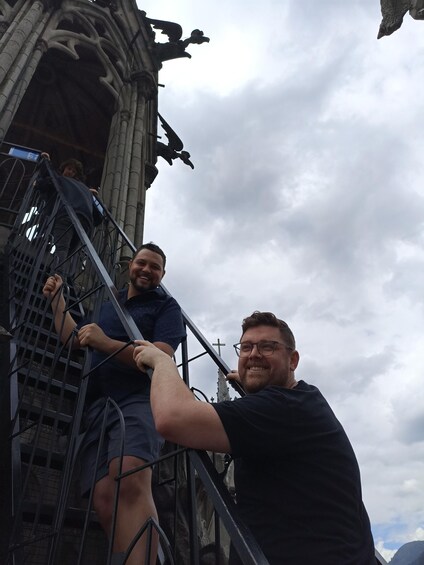 Two people climbing a metal staircase with gothic architecture in the background. 4