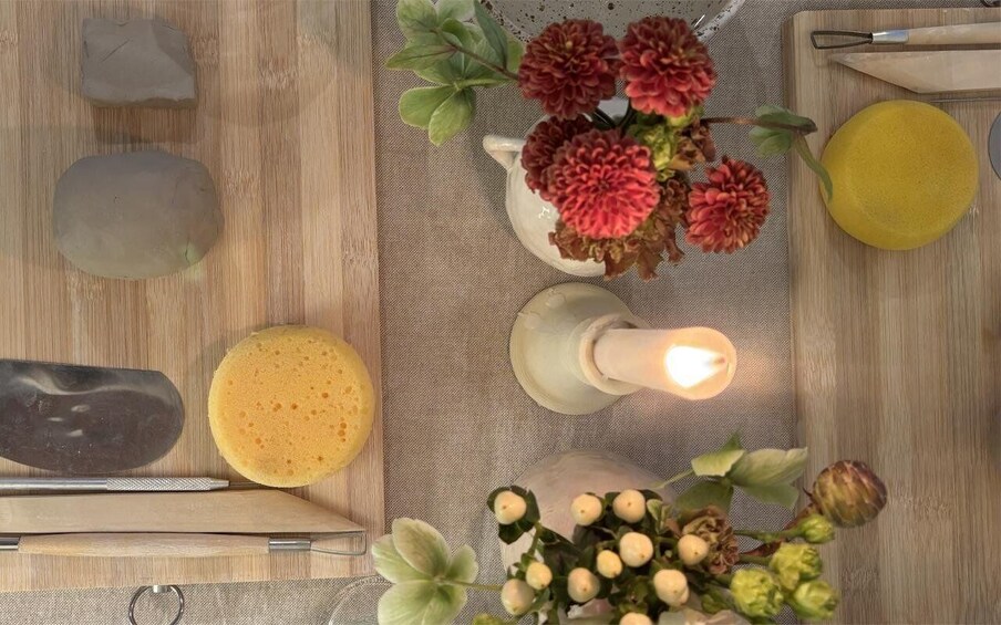 A wooden surface with a candle, flowers, a yellow bowl, a sponge, and a knife. 4