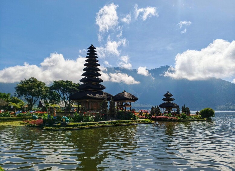 A serene lake with traditional tiered pagodas and thatched-roof structures amidst lush greenery and a clear sky. 3