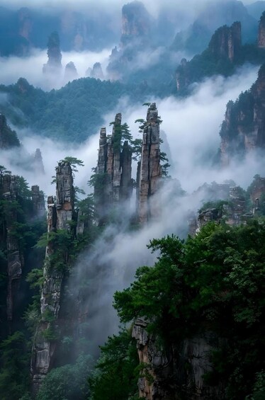 A misty mountain landscape with towering rock formations and dense green foliage. 1