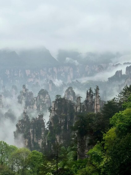 A misty mountain landscape with towering rock formations and dense green foliage. 4