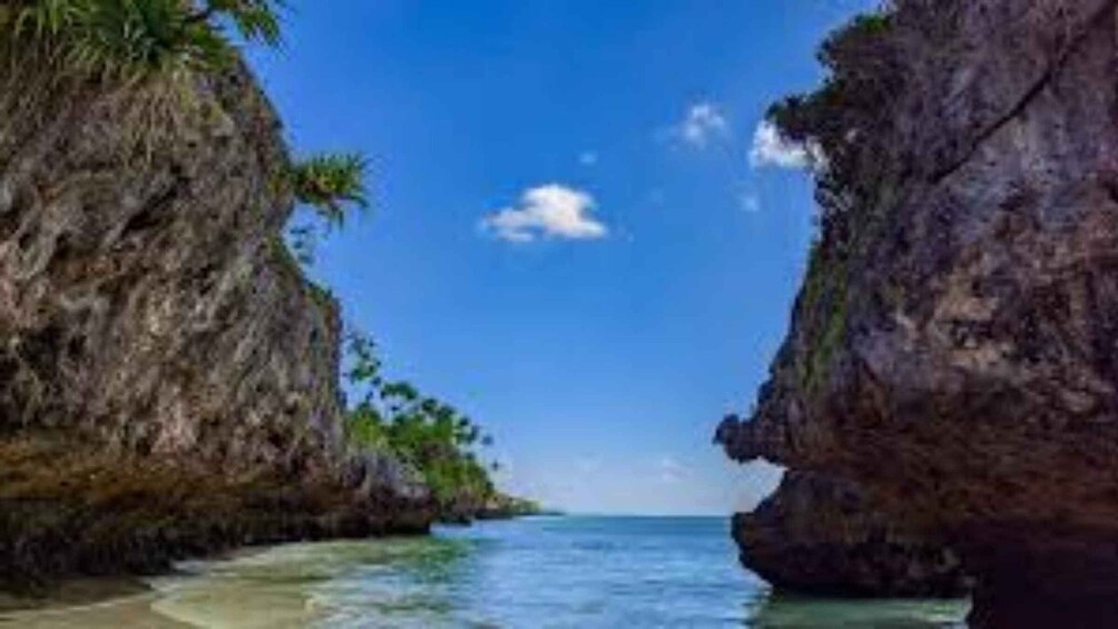 A coastal landscape with a narrow waterway flanked by rocky cliffs and palm trees. 5